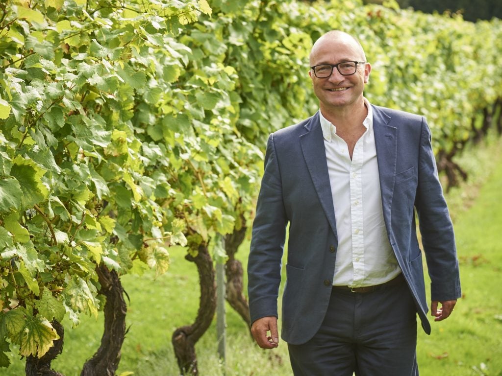 Andrew Carter poses smiling next to a row of vines