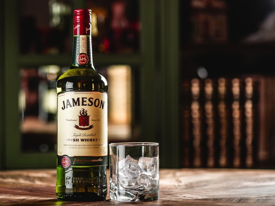 A bottle of Jameson whiskey and a glass with ice cubes sat on a bar