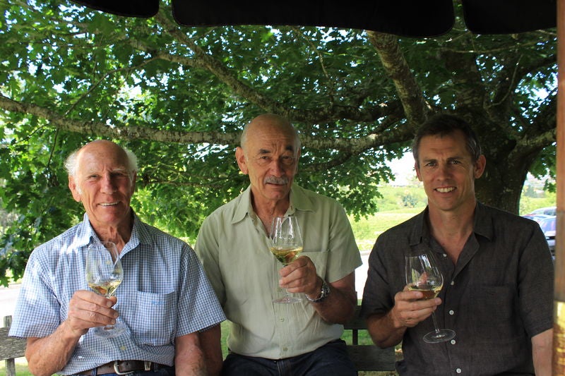 Three members of the Babich Wines family in New Zealand hold glasses of white wine sat under a tree