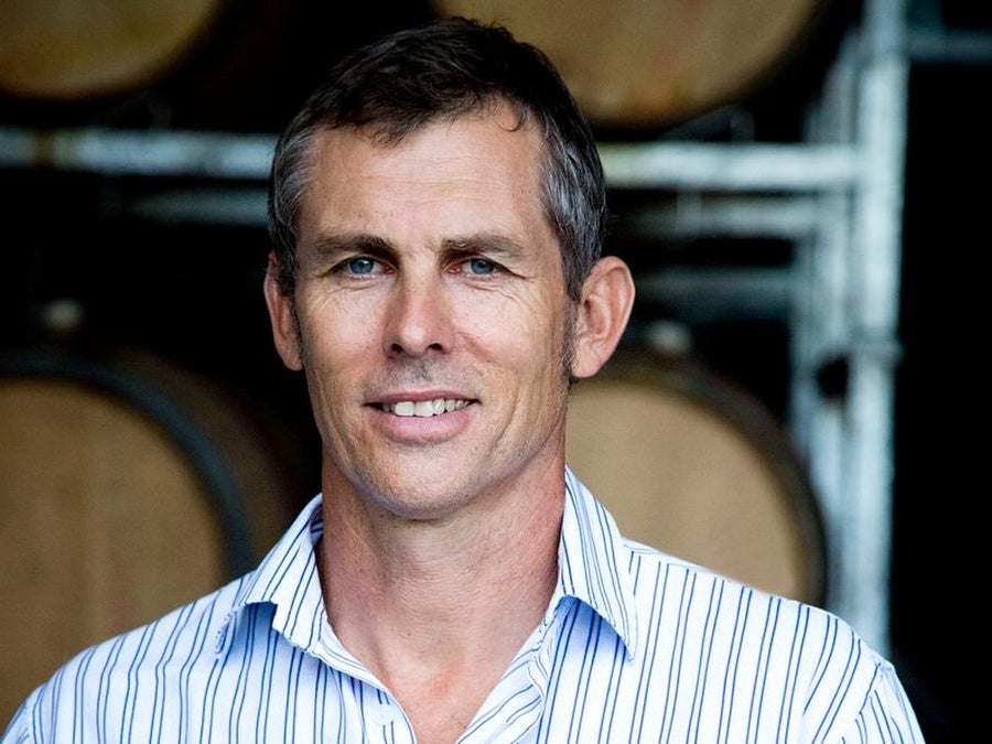 David Babich smiles and leans against a stack of wine barrels