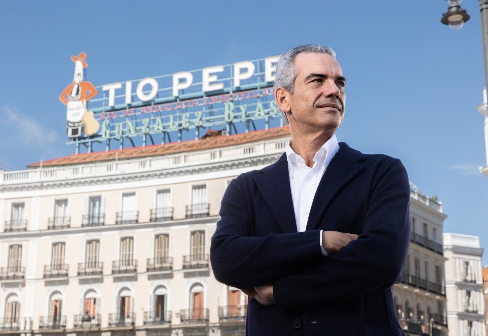 A white man with grey hair stands in front of a Tio Pepe sign atop a six-story building in Spain