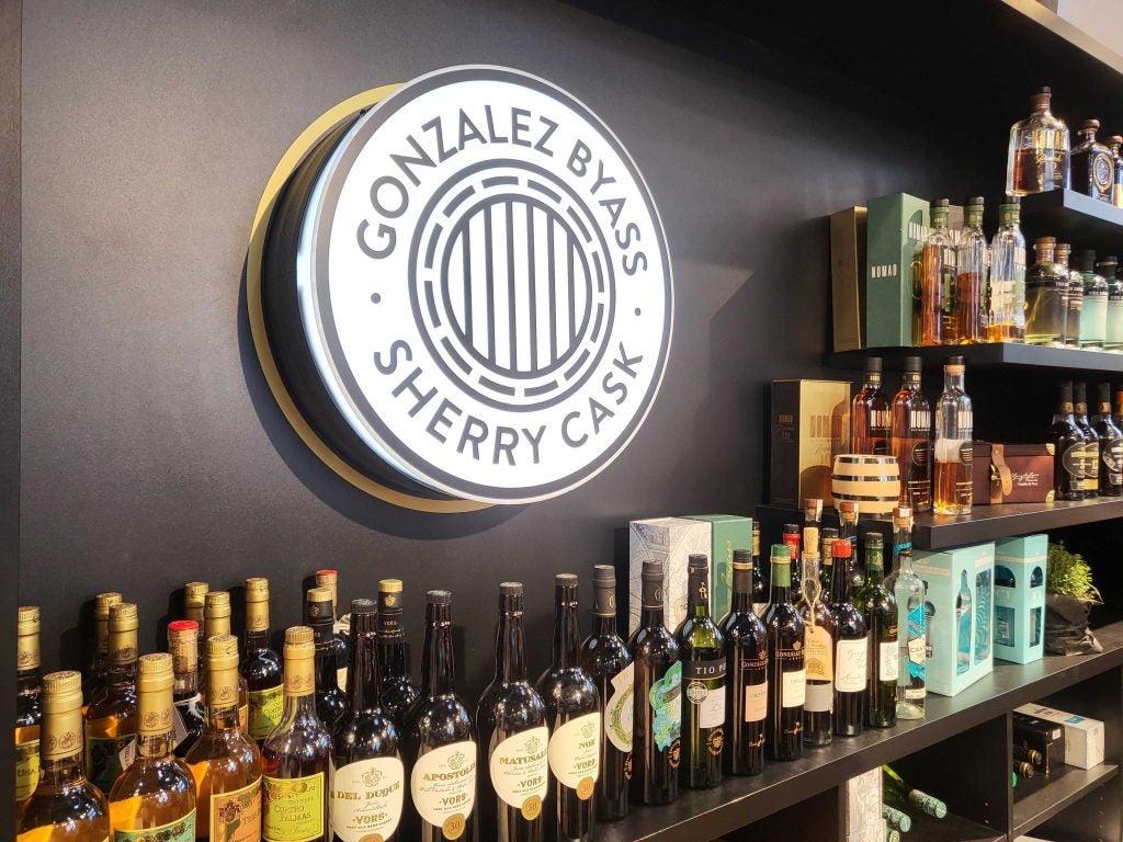 A shelf of spirits under a large round lit-up sign reading Gonzalez Byass