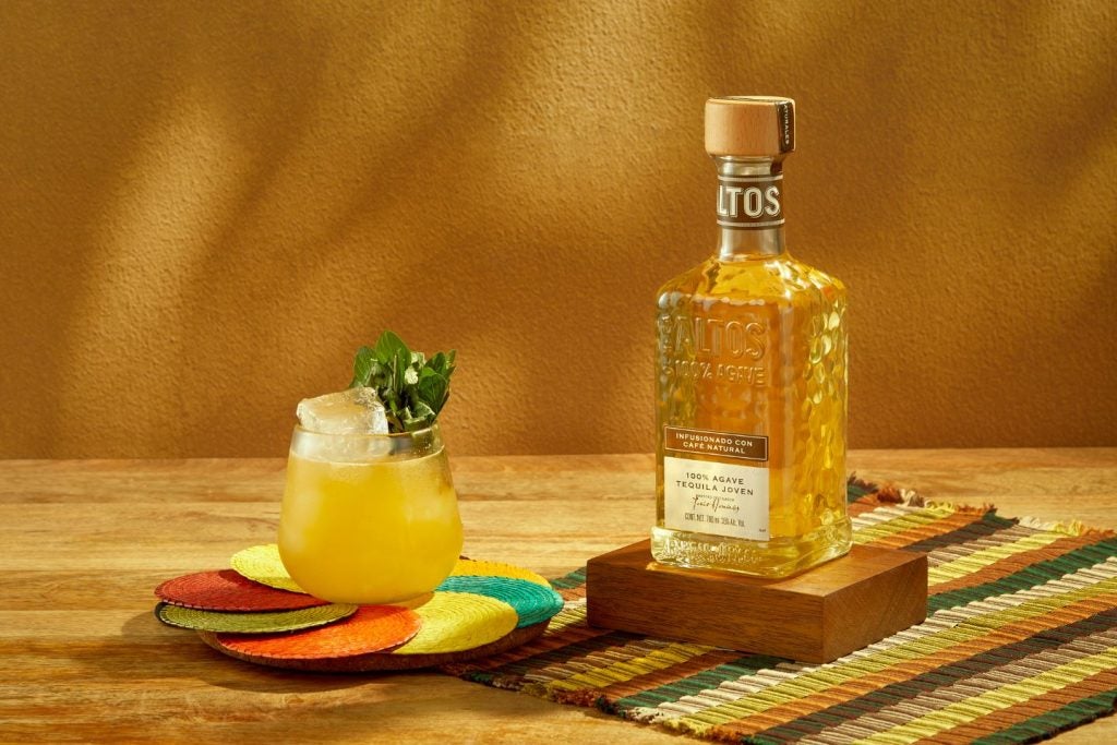 Coffee-infused tequila bottle and glass of tequila-based cocktail on multi-coloured coaster.