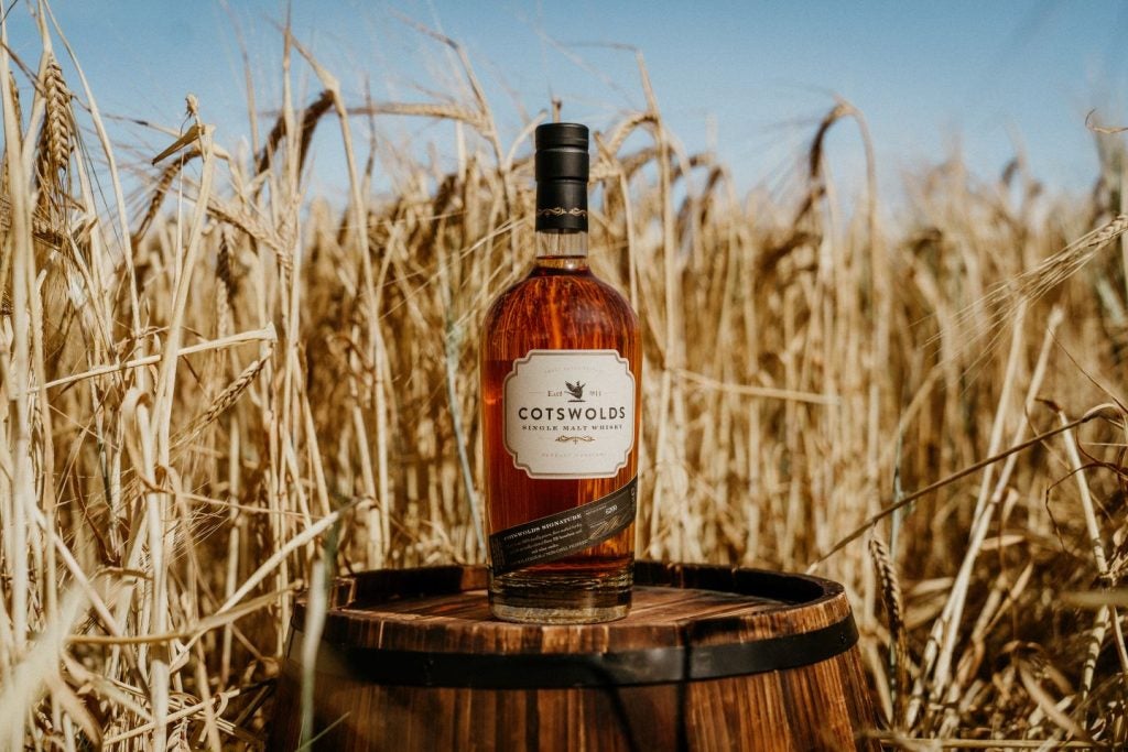 Bottle of English whisky, Cotswolds Distillery brand on barrel in wheat field.