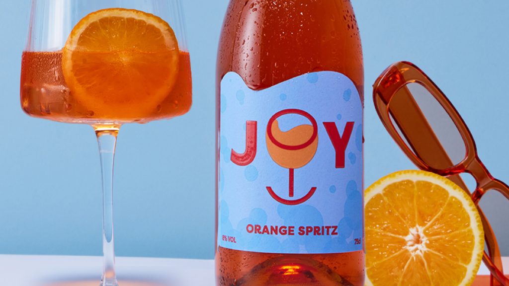 orange wine bottle next to glass with orange spritz and orange slice. Blue background