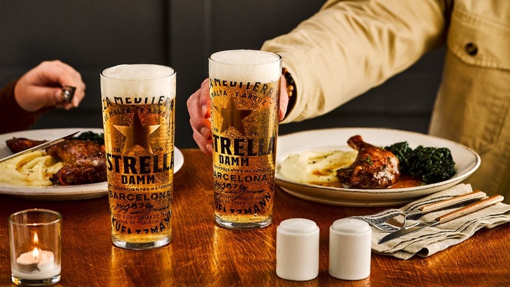 two pints of beer in Estrella Damm branded glasses alongside meal on wooden table.