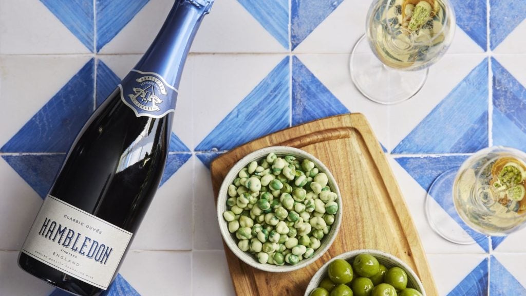 bottle of sparkling wine on blue and white tiles with salty snacks and glasses of sparkling wine.