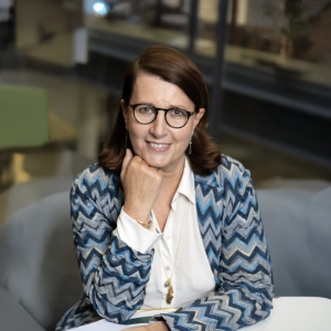 Woman wearing glasses smiling at camera in blue cardigan and white shirt.