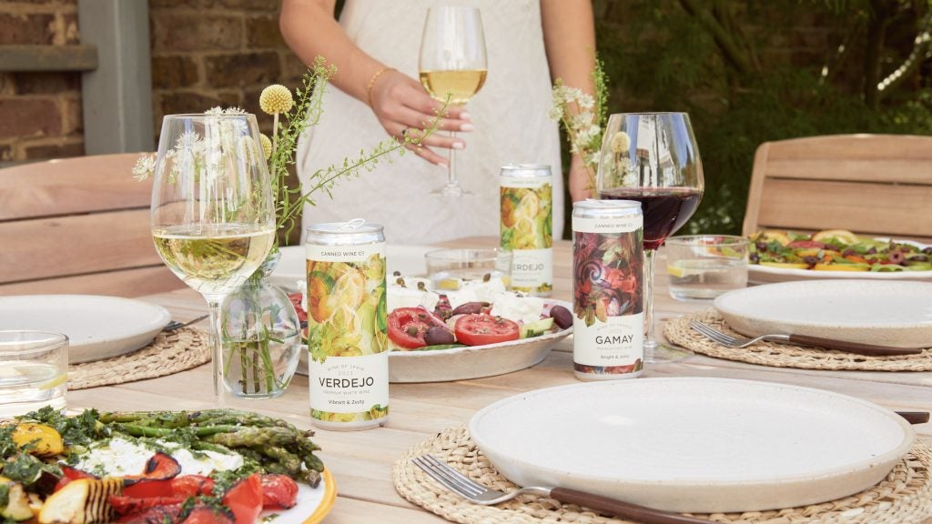 Cans of wine and white plates, food on table.