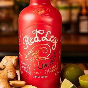 RedLeg branded red bottle of spiced rum on bar next to ginger and lime slices.