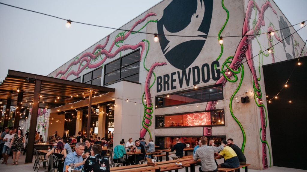 Beer taproom, BrewDog name painted on building, benches outside with fairy lights.