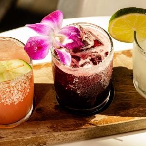 Selection of three margarita cocktails with garnishes on wooden slate.
